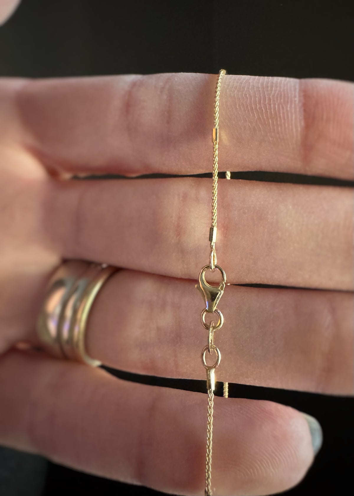 close up of a 14k yellow gold chain necklace showing the lobster style clasp on a hand with a black background