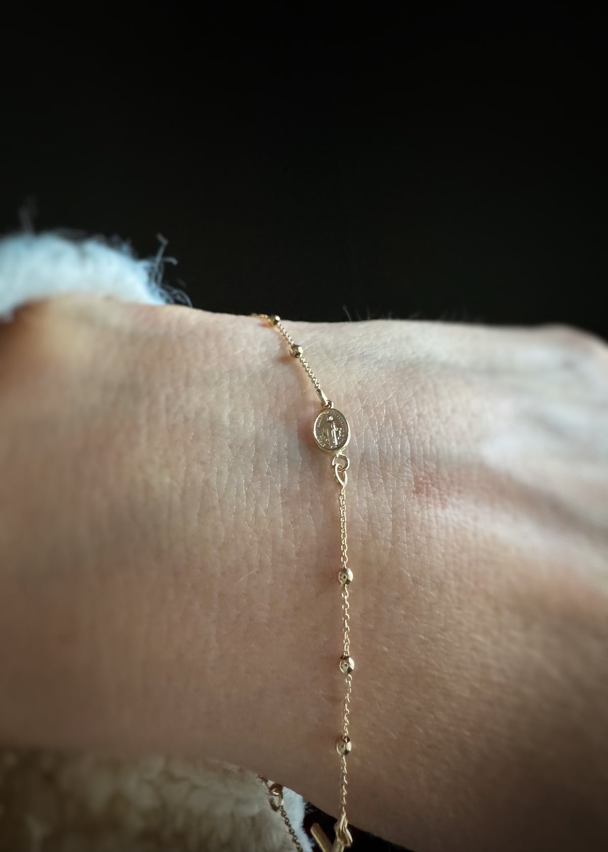 14k yellow gold rosary bracelet on a wrist with a dark background