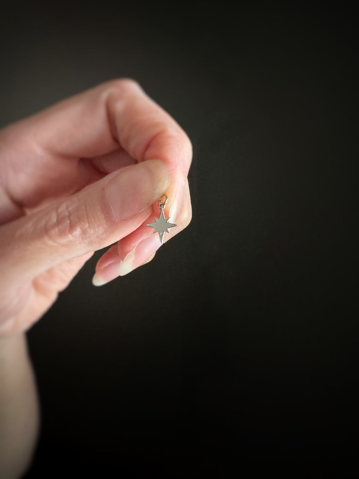 Hand holding a small 14k white gold celestial star charm, showing the backside of the charm against a dark background