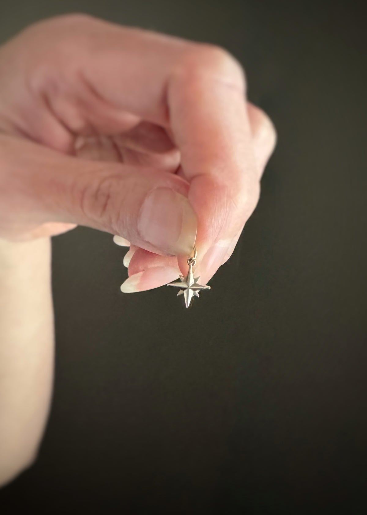 Hand holding a small 14k white gold celestial star charm against a dark background
