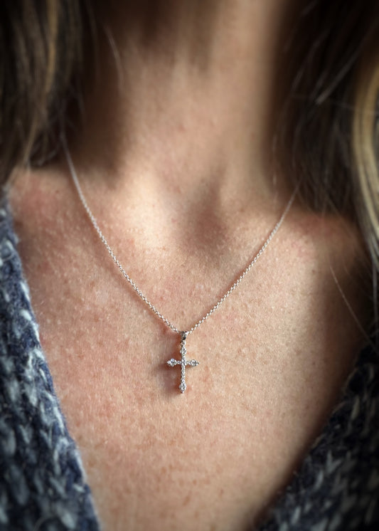 Close-up of a person wearing a white gold and diamond cross necklace.