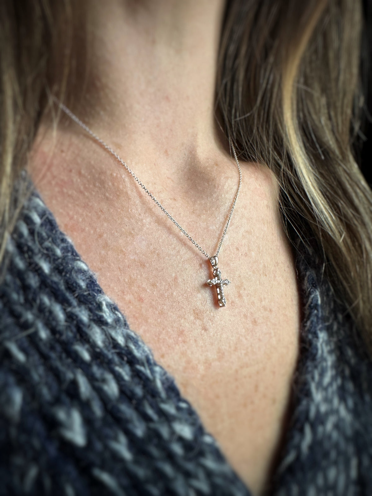 side view of a 14k white gold and diamond cross pendant worn by a person