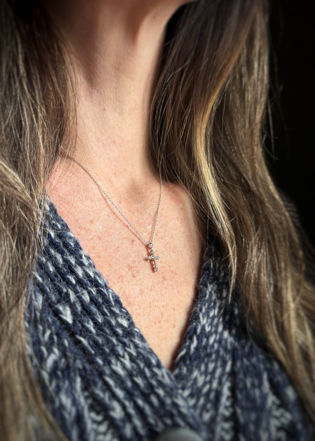 Close-up of a person wearing a white gold diamond cross necklace, blurred background