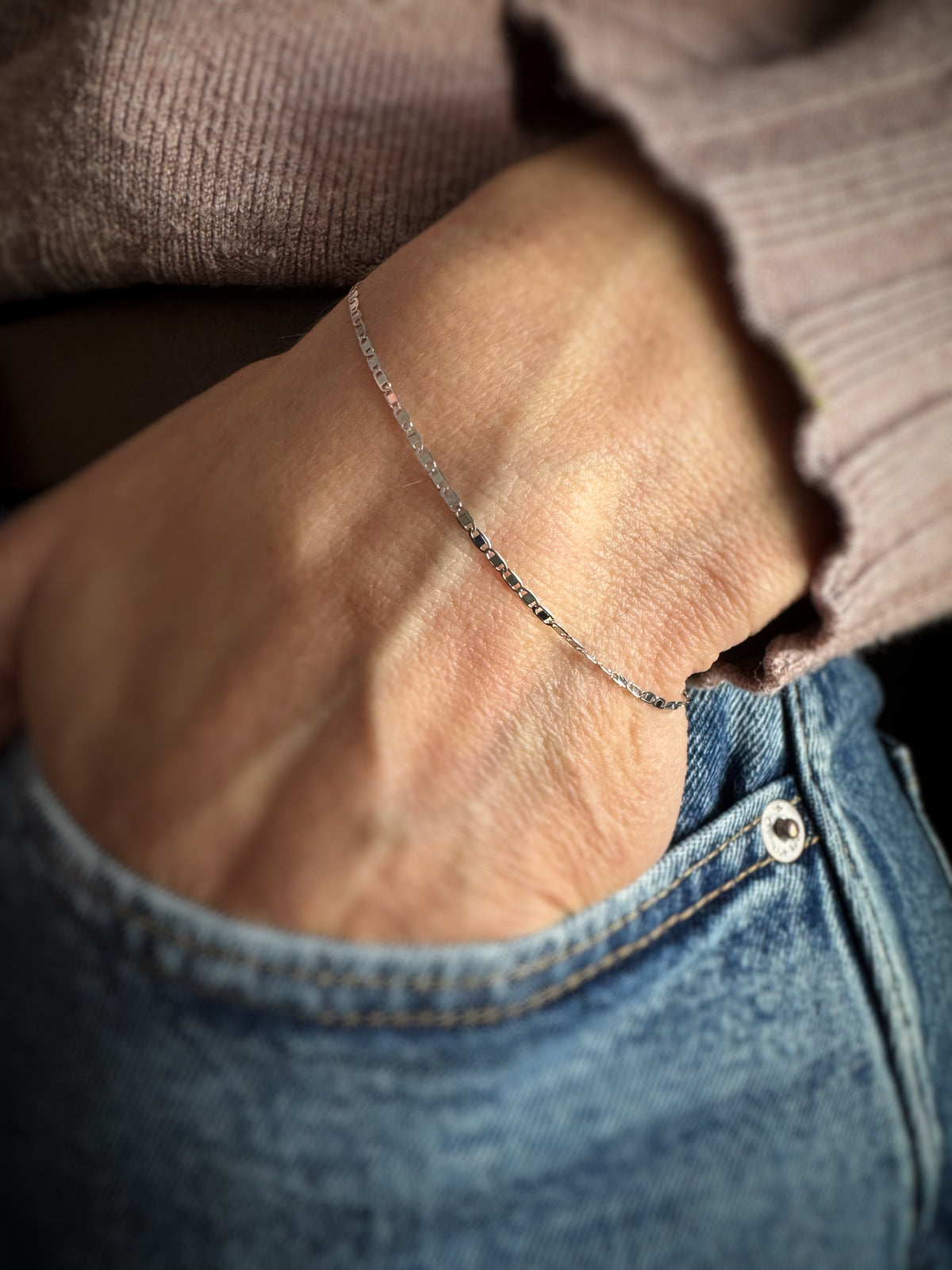 Close-up of a person wearing a 14k white gold mirror chain bracelet on a blurred background