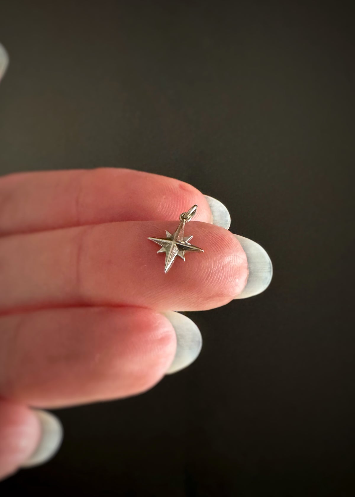 Small 14k white gold celestial star charm held on the tip of someone's finger against a dark background