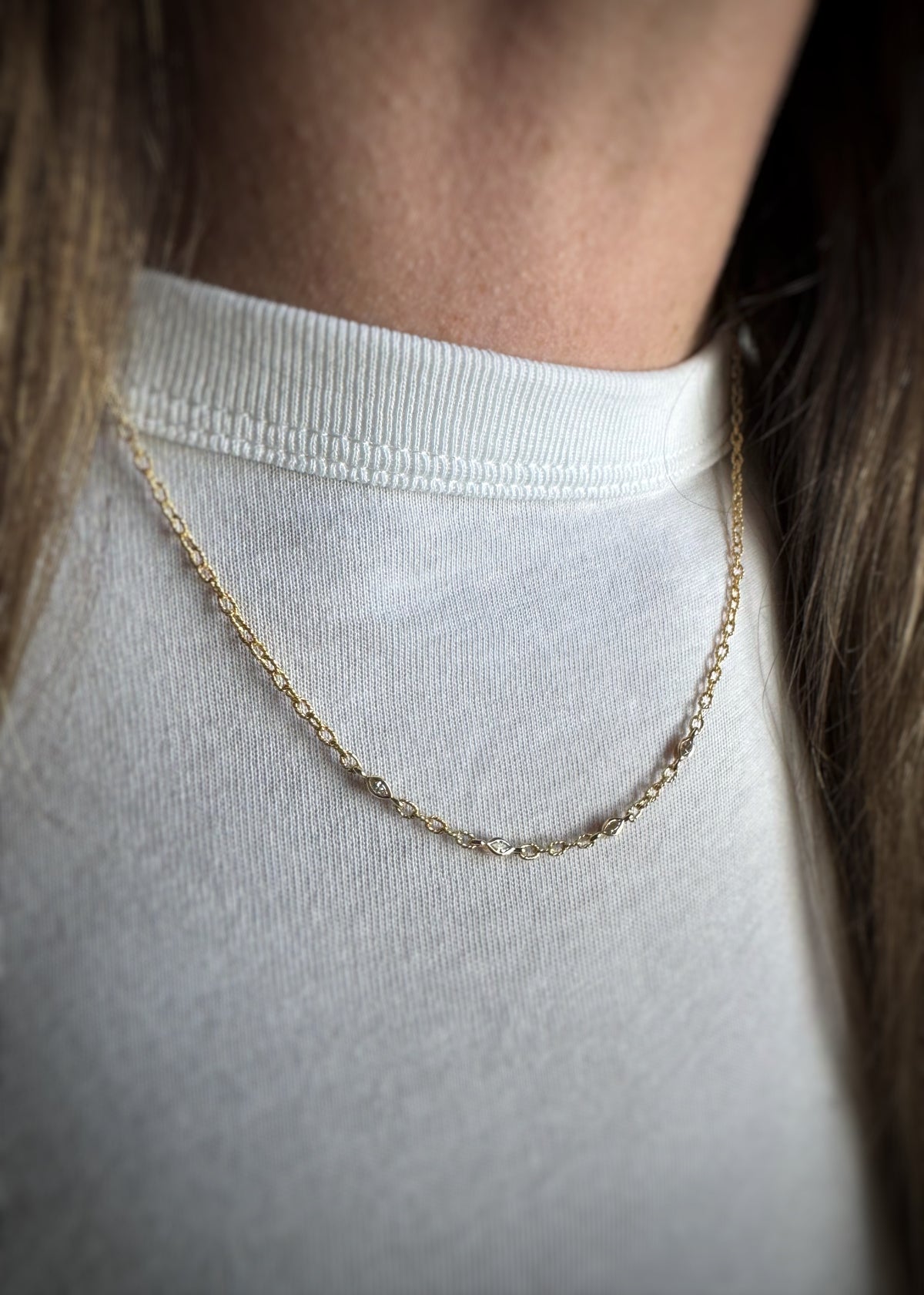 yellow gold chain with four bezel set marquise diamonds stationed into the chain worn by a person in a white shirt