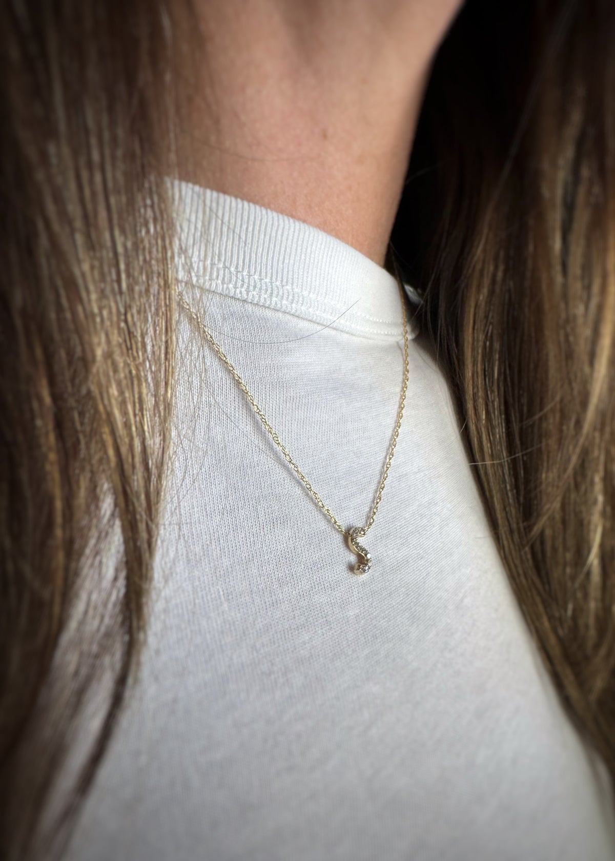 yellow gold necklace with a small diamond accented letter S pendant worn by a person against a white background