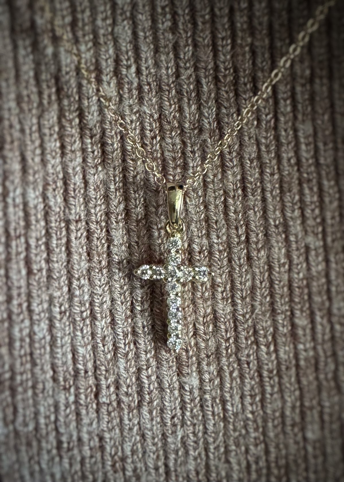 yellow gold cross necklace with diamonds on a textured surface