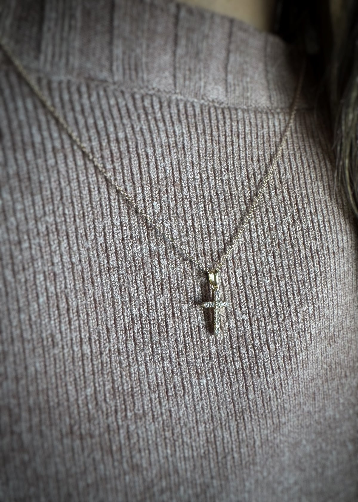 yellow gold necklace with a diamond cross pendant on a gray textured fabric background
