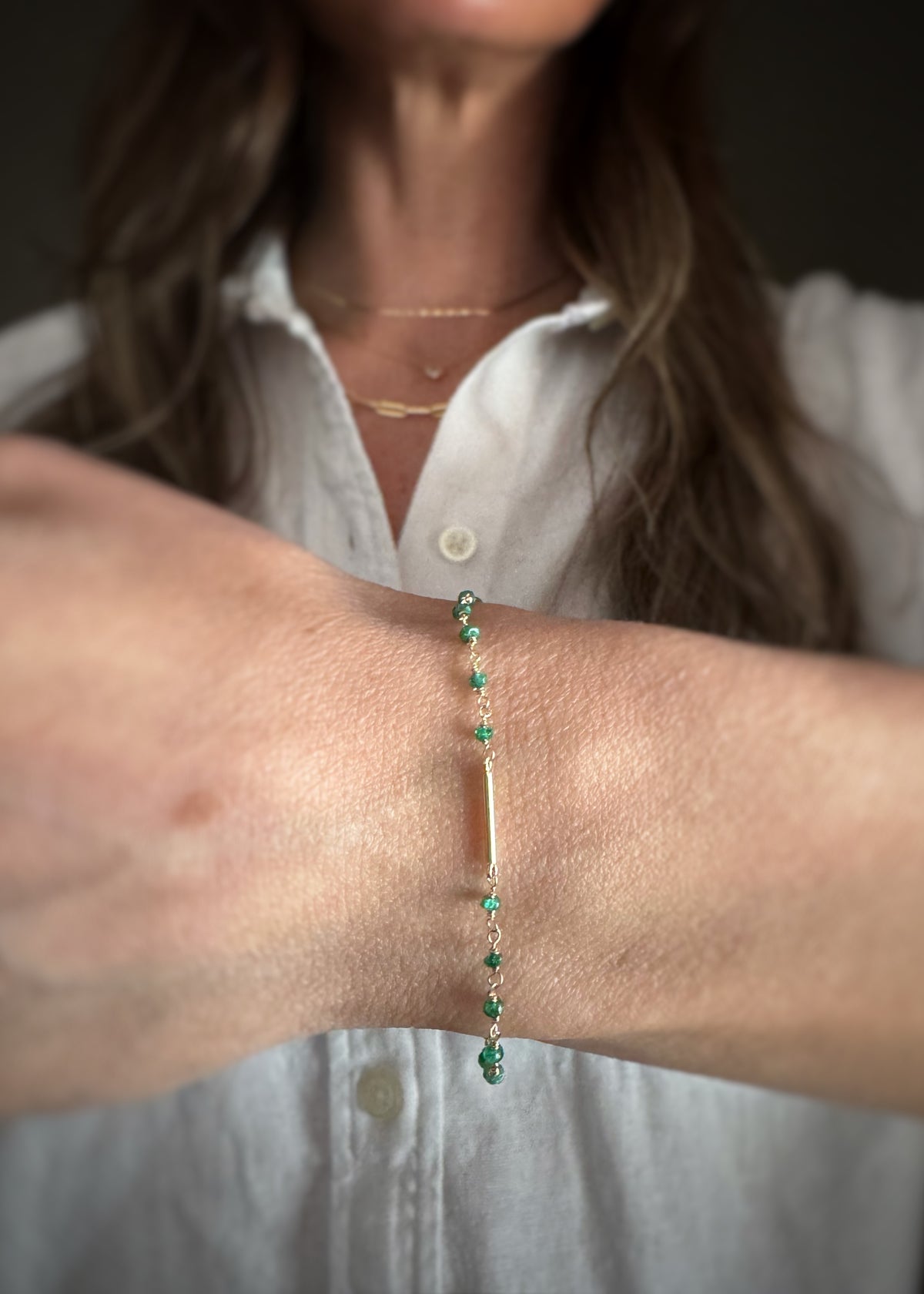 Person wearing a green emerald bead chain bracelet with a bar in the center on a neutral background