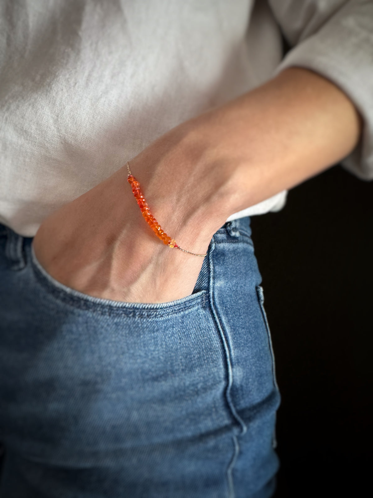 Person wearing a vibrant orange mexican fire opal gemstone bead bracelet on a neutral background