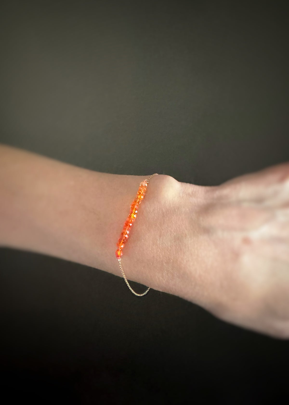 Close-up of a wrist wearing a vibrant orange beaded bracelet against a dark background