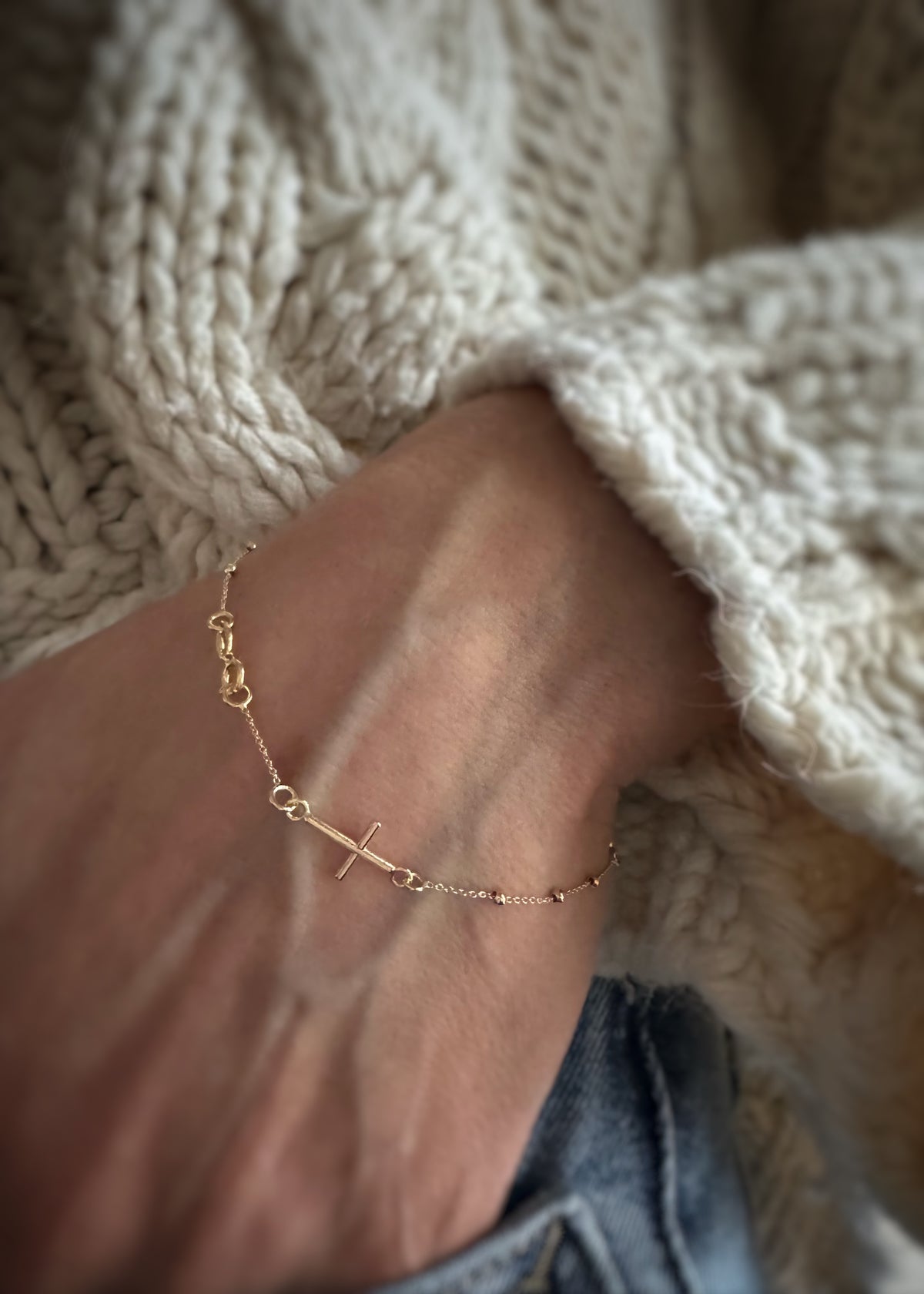 14k yellow gold rosary bracelet on a wrist with a textured white sweater background