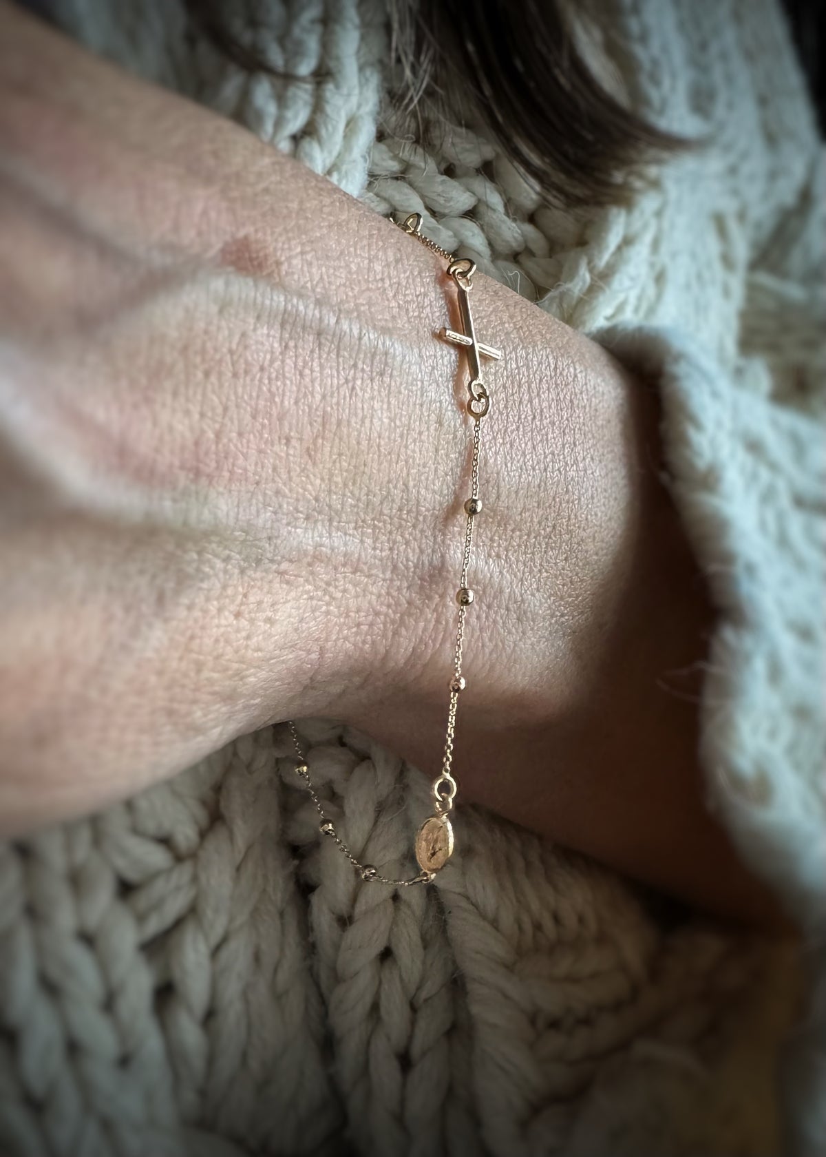close-up of a 14k gold rosary chain bracelet on a person's ankle with a soft background