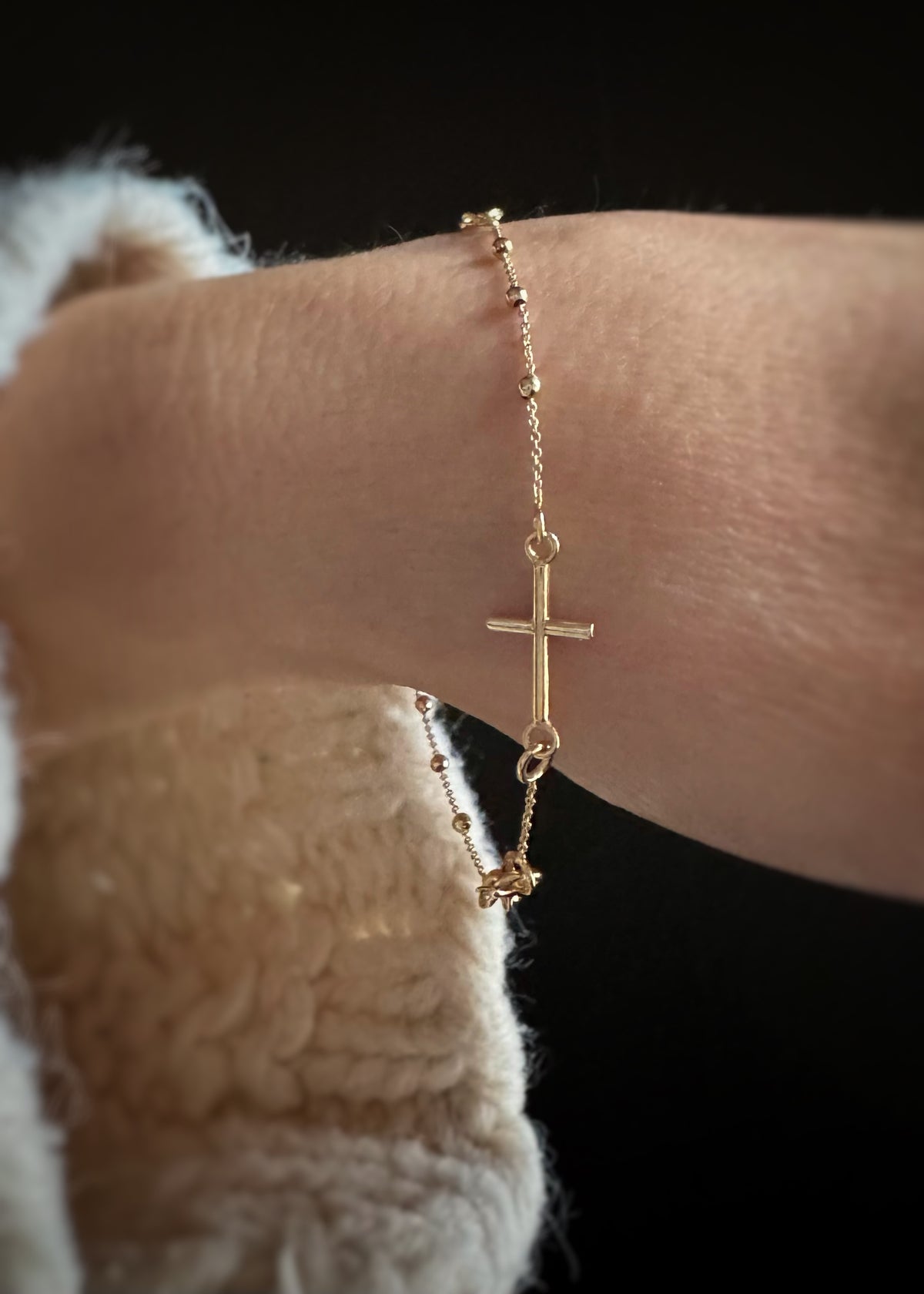 14k Gold bracelet with a cross on a wrist against a dark background
