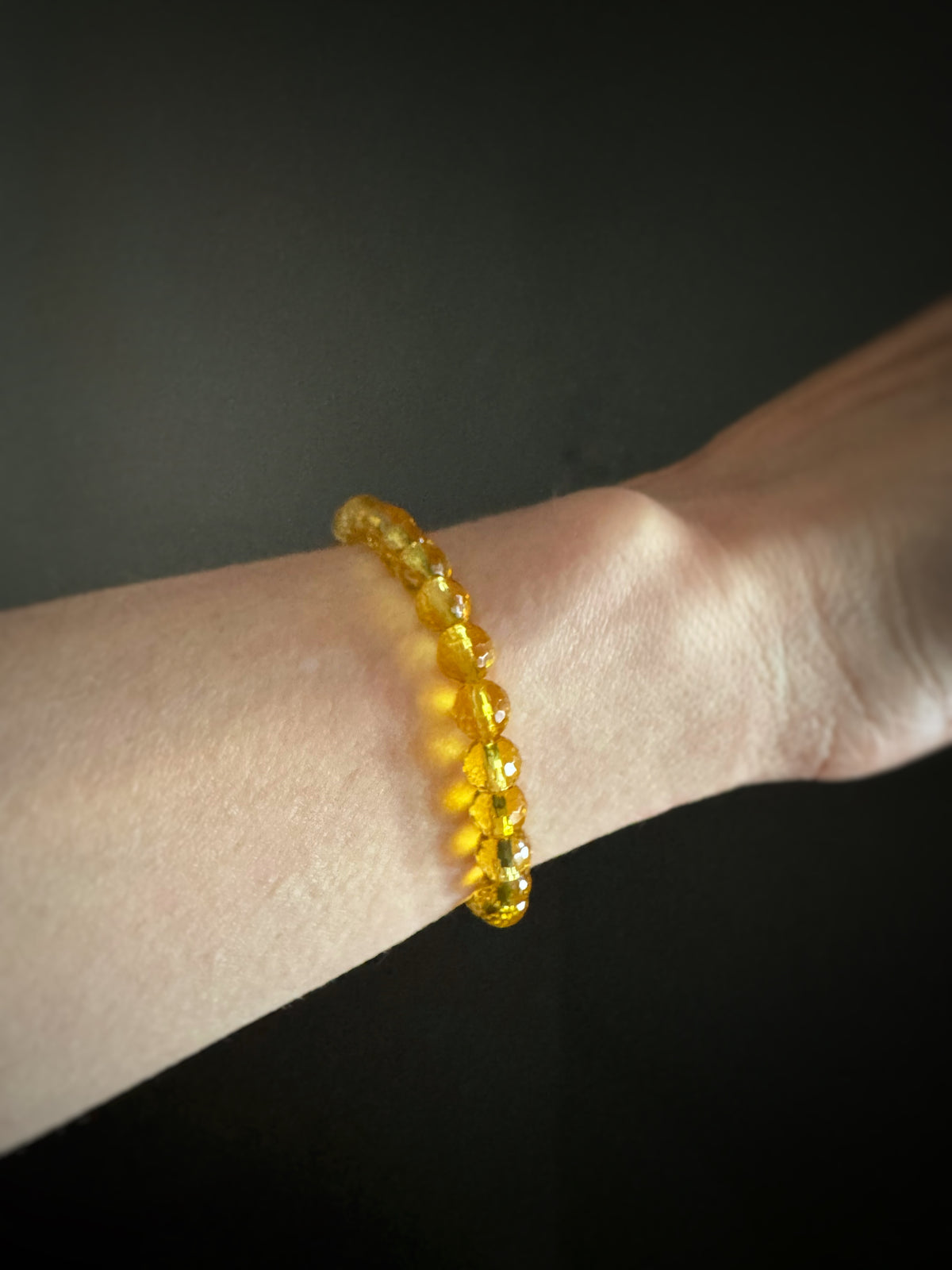 faceted round citrine beaded elastic stretch bracelet on a wrist against a dark background