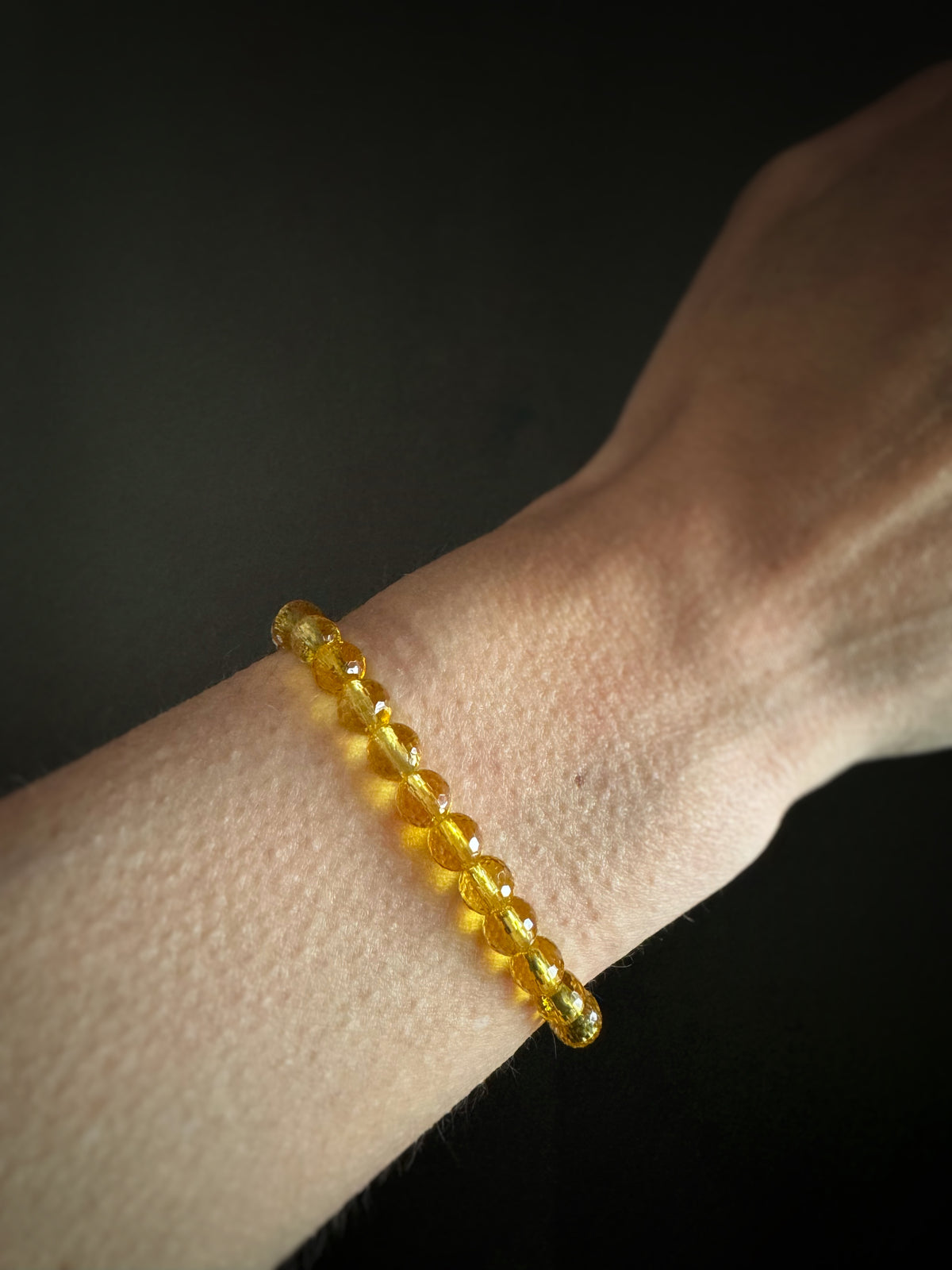 Yellow faceted citrine beaded elastic stretch bracelet on a wrist against a dark background