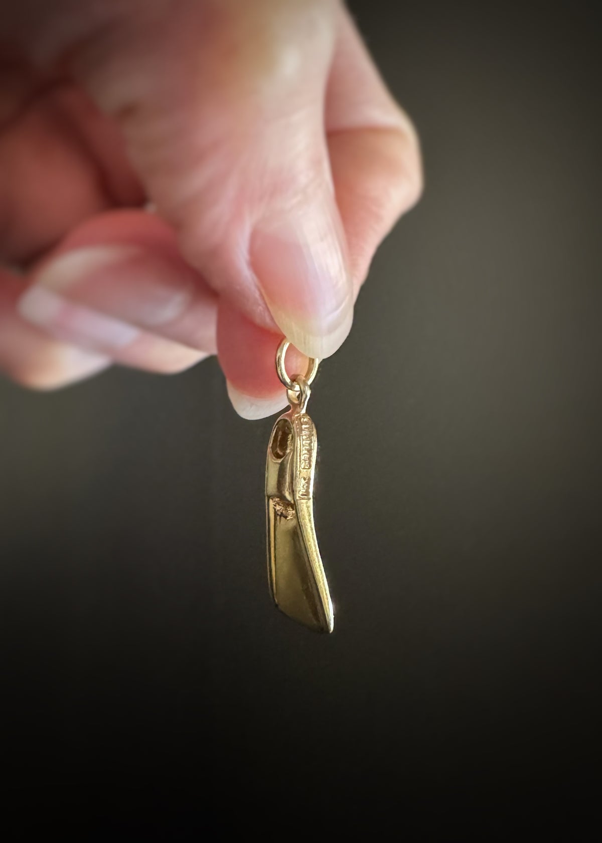 side view of an preowned 14 karat gold flipper charm marked "14k BAHAMAS" held by a hand against a dark background