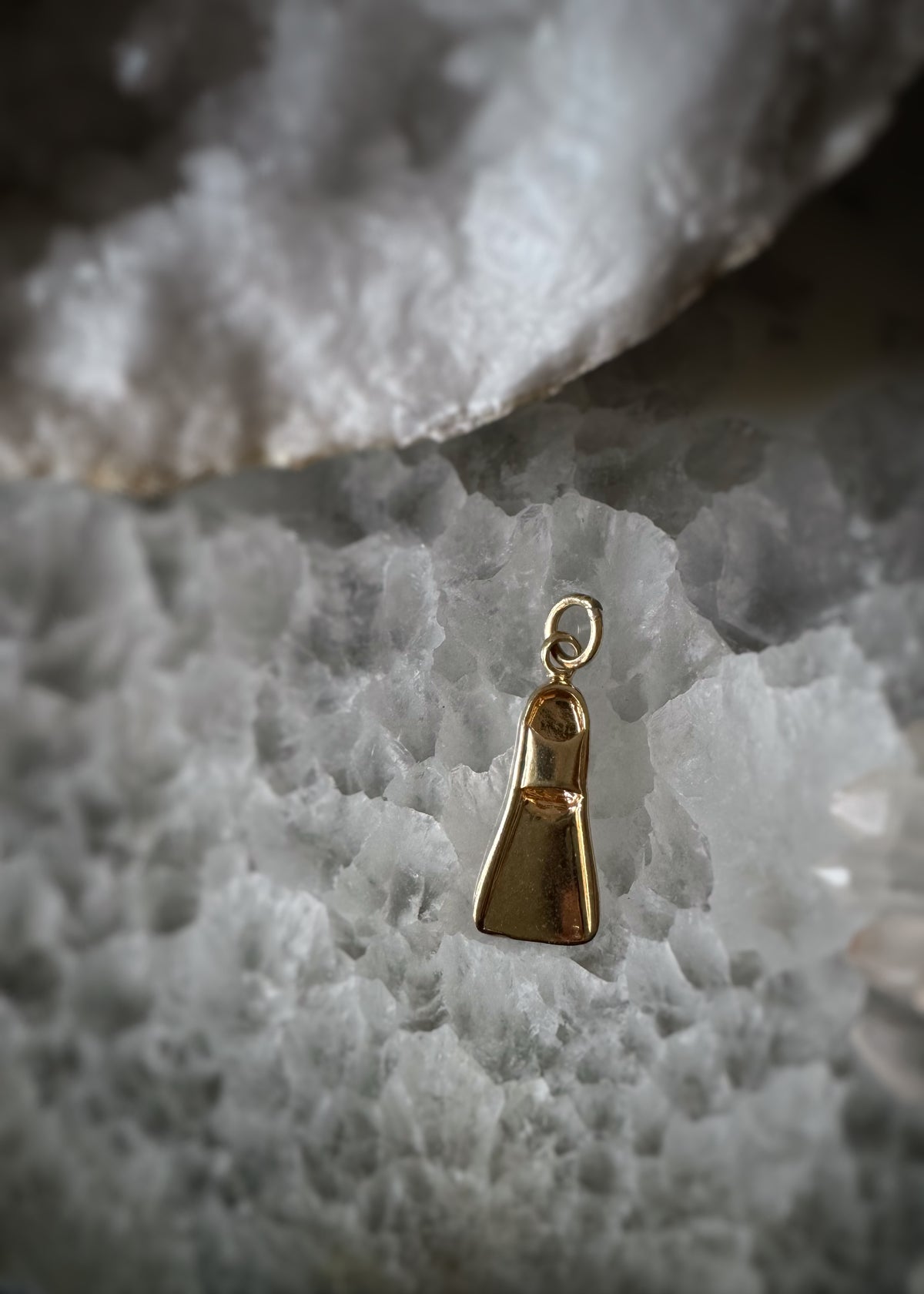 top view of an estate 14k yellow gold flipper bracelet charm on a textured white surface
