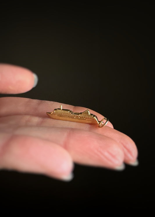 pre-owned 14k yellow gold "Silver Whisper" cruise ship charm on a hand against a dark background