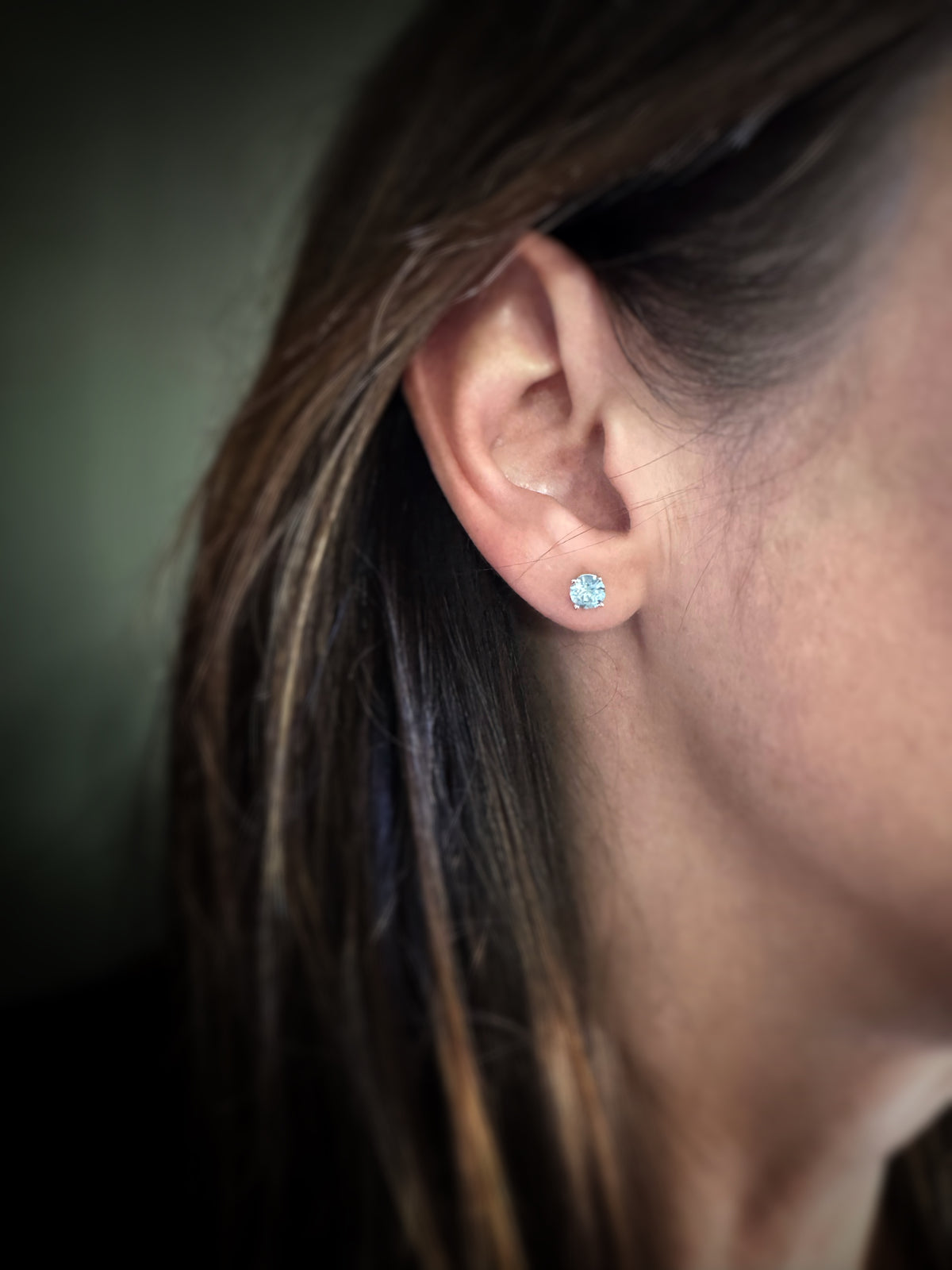 Close-up of a person wearing a blue topaz earring set in 14k yellow gold with a blurred background