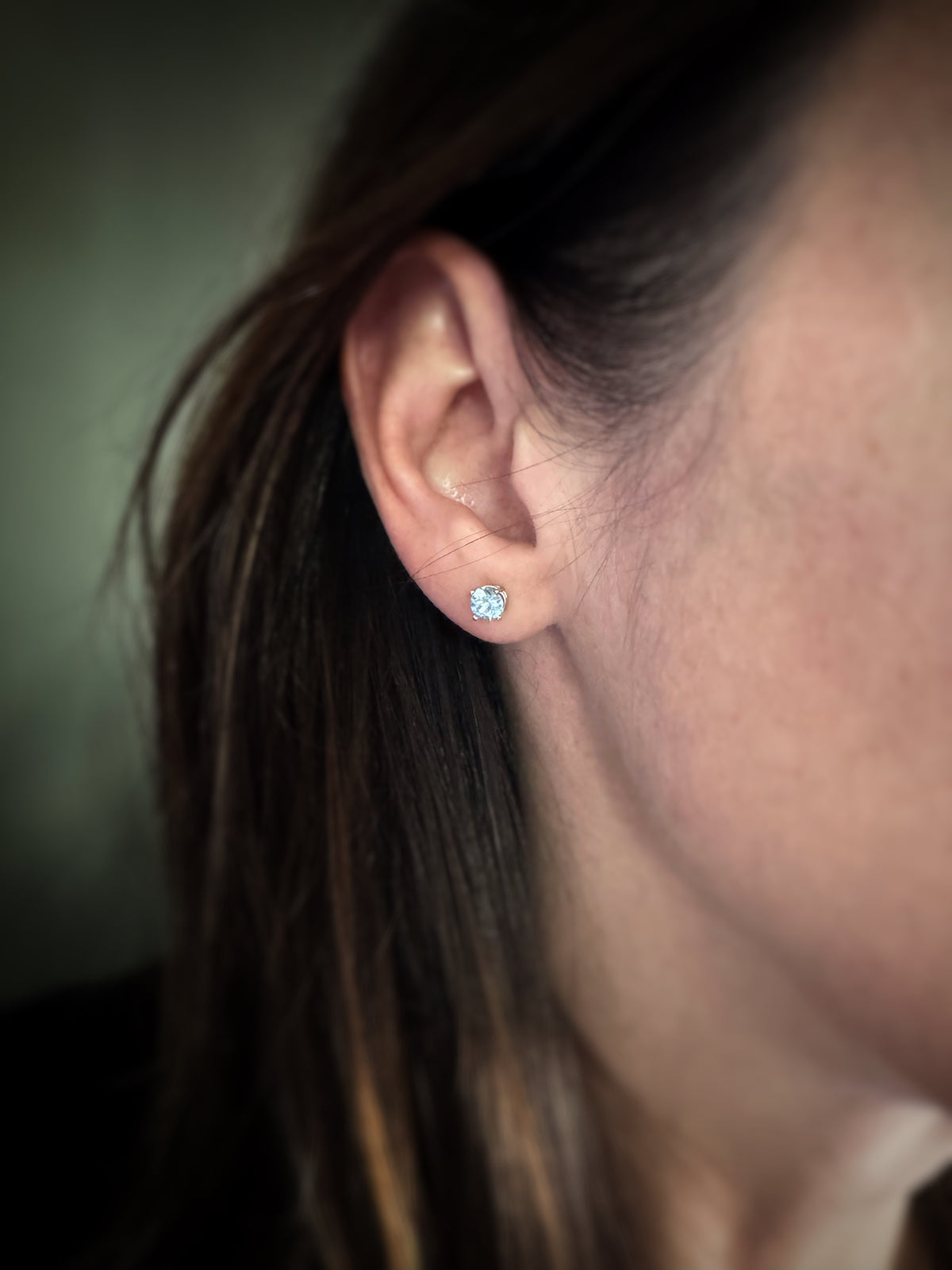 Close-up of a person wearing a gold round blue topaz stud earring with a blurred background