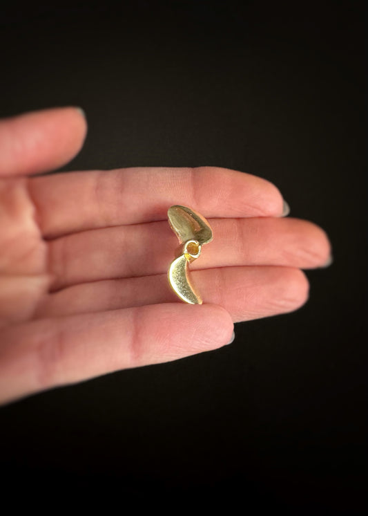 Estate 14k yellow gold boat propeller pendant held between fingers against a dark background