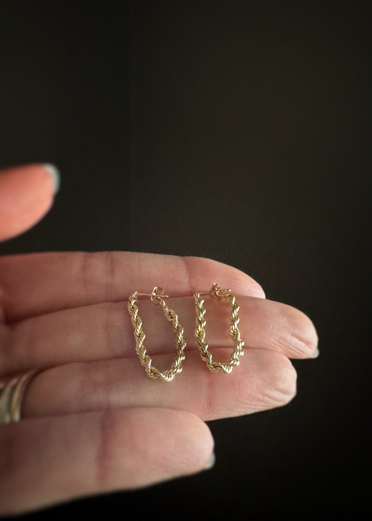 14k yellow gold rope chain hoop earrings held on top of a person's fingers against a dark background