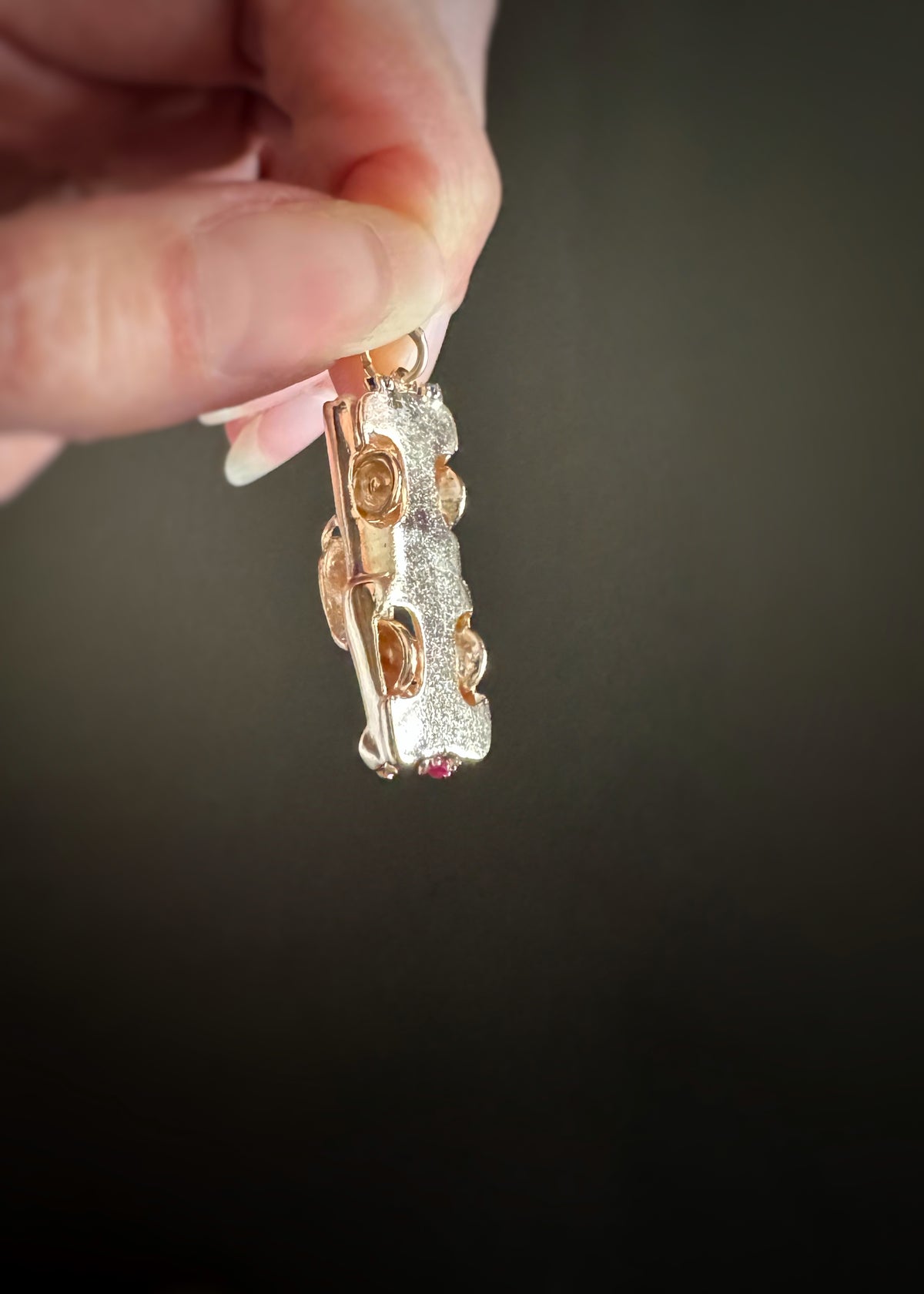 14 karat yellow gold classic car charm held by a hand to show the bottom of the charm against a dark background