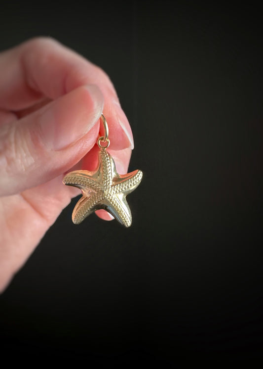 Estate 14k yellow gold large starfish charm held by a hand against a black background