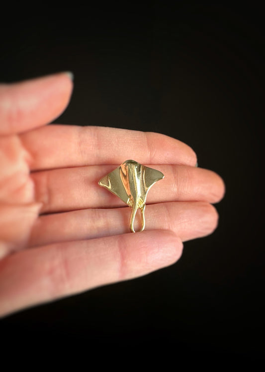 pre-owned yellow gold stingray-shaped pendant held in a hand against a black background