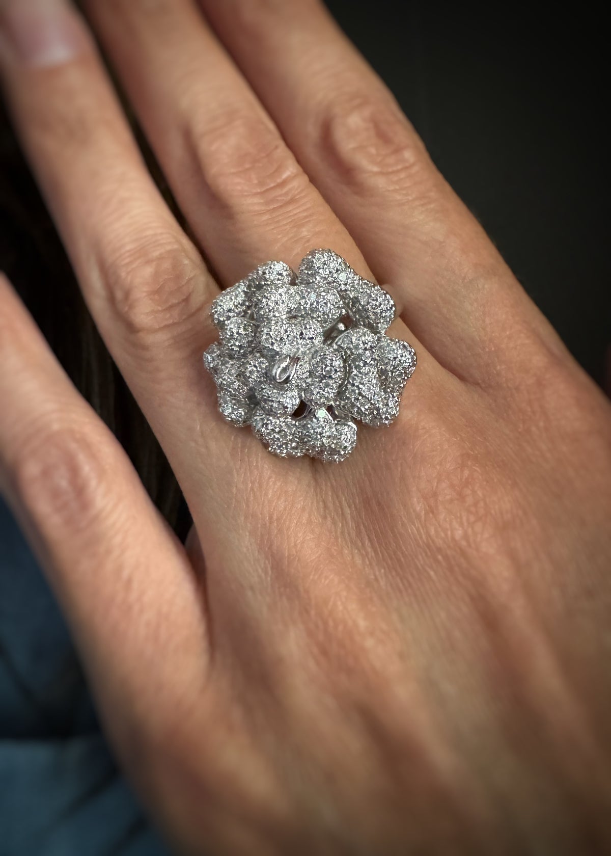A close-up of a hand wearing an estate  18k white gold large cocktail ring adorned with numerous small diamonds.