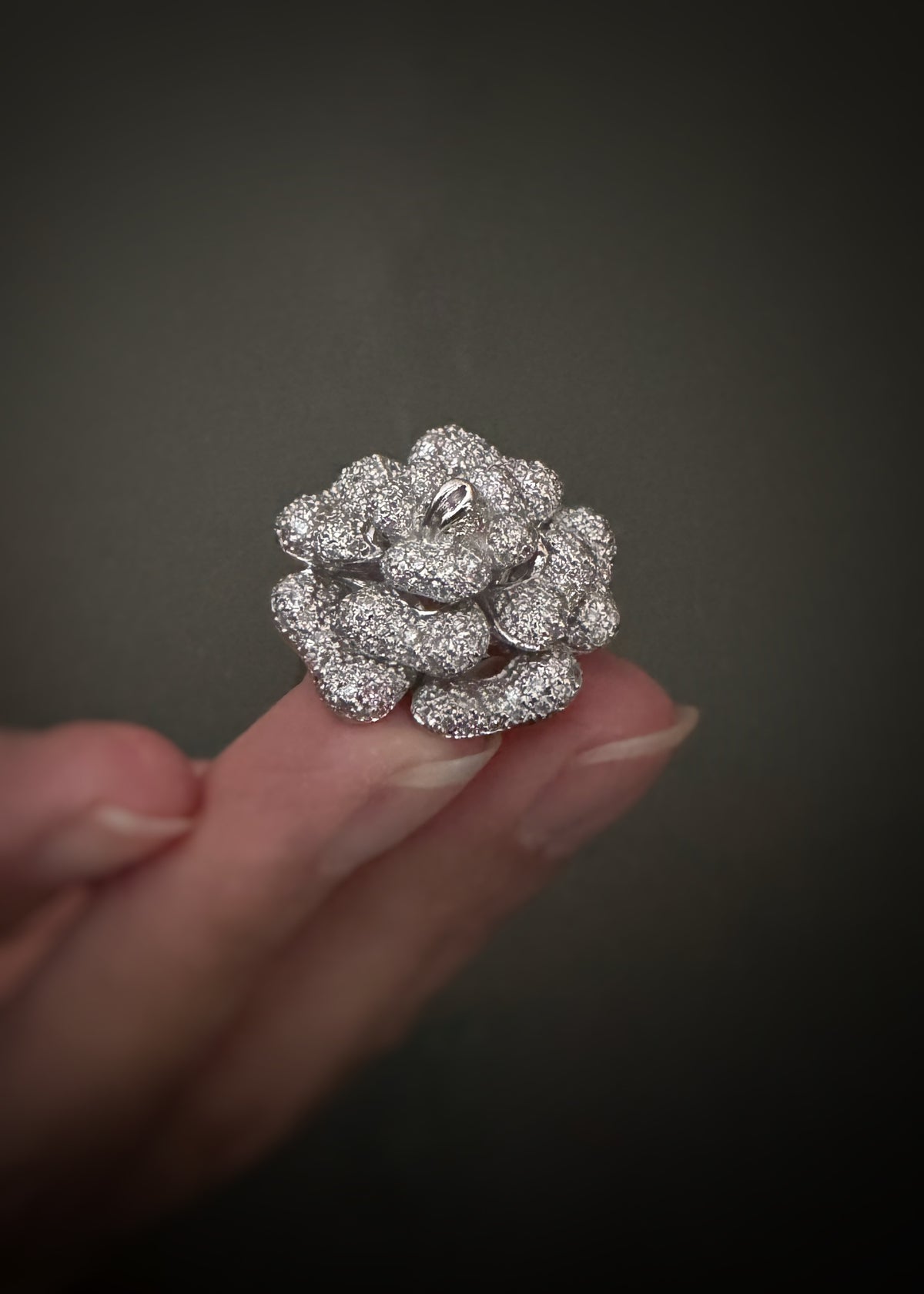 A close-up of a hand holding an estate 18k white gold cocktail ring with a cluster of pavé-set diamonds against a dark gray background.