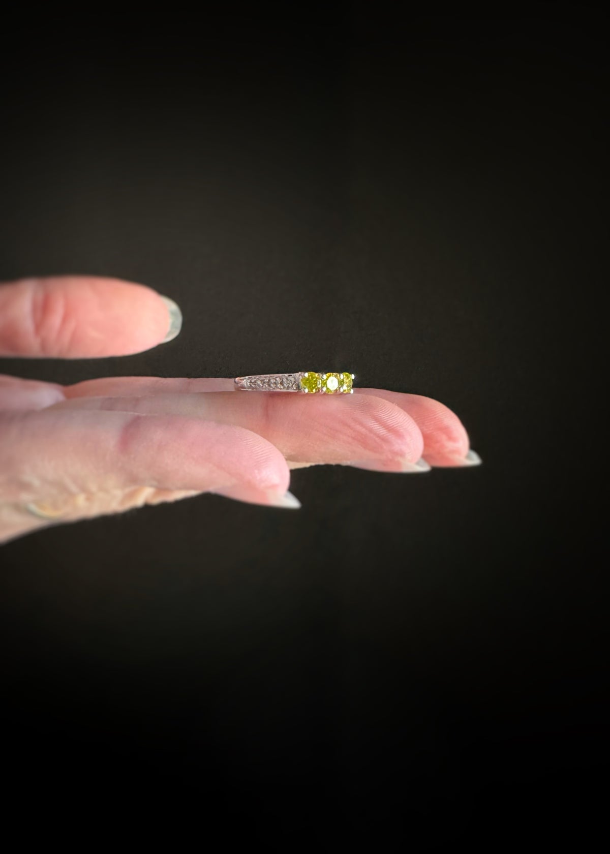 estate 18k white gold ring with three yellow diamonds in the center with white diamond accents sitting flat on the model's fingers against a black background