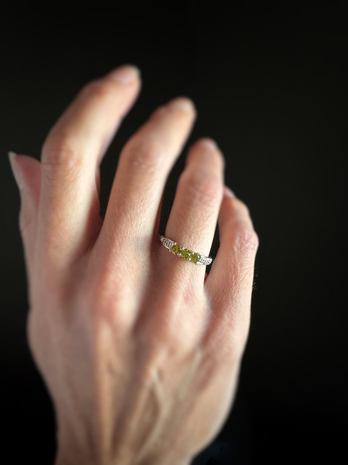 Hand wearing a estate 18 karat white gold ring with three yellow diamonds against a black background
