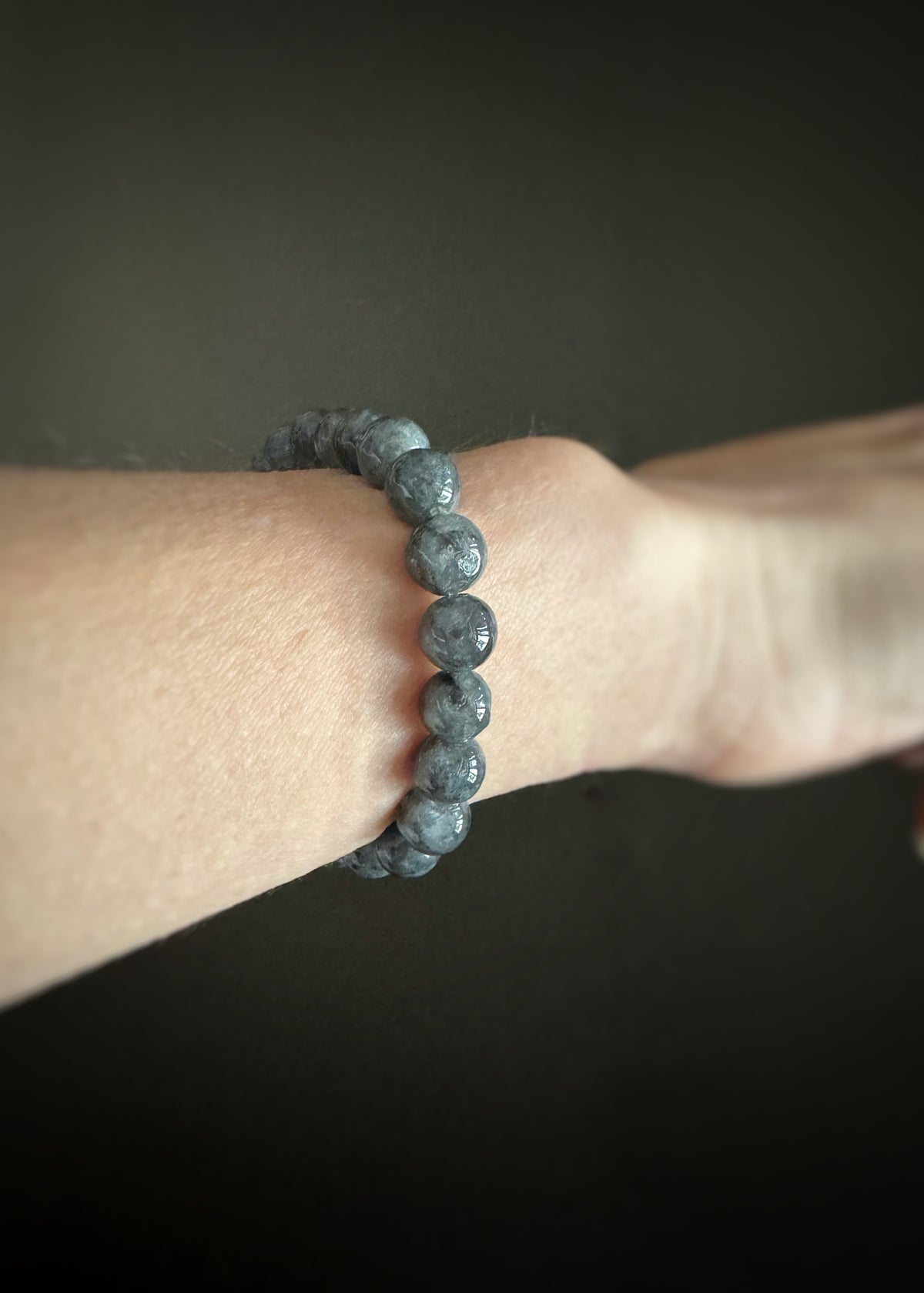 blueish gray labradorite round beaded bracelet on a wrist against a dark background