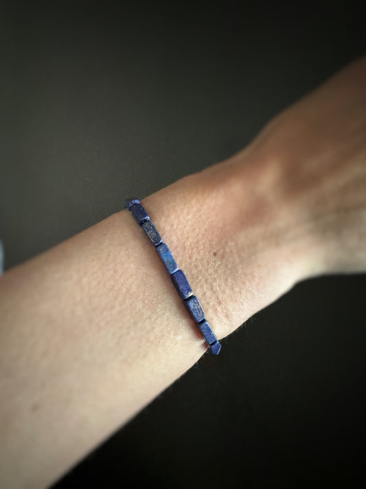 Royal blue rectangular lapis beads strung on stretchy cord bracelet on a wrist against a dark background