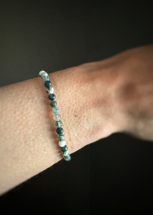 Close-up of a wrist wearing a smooth round moss agate bead bracelet strung on stretchy cord with a dark background