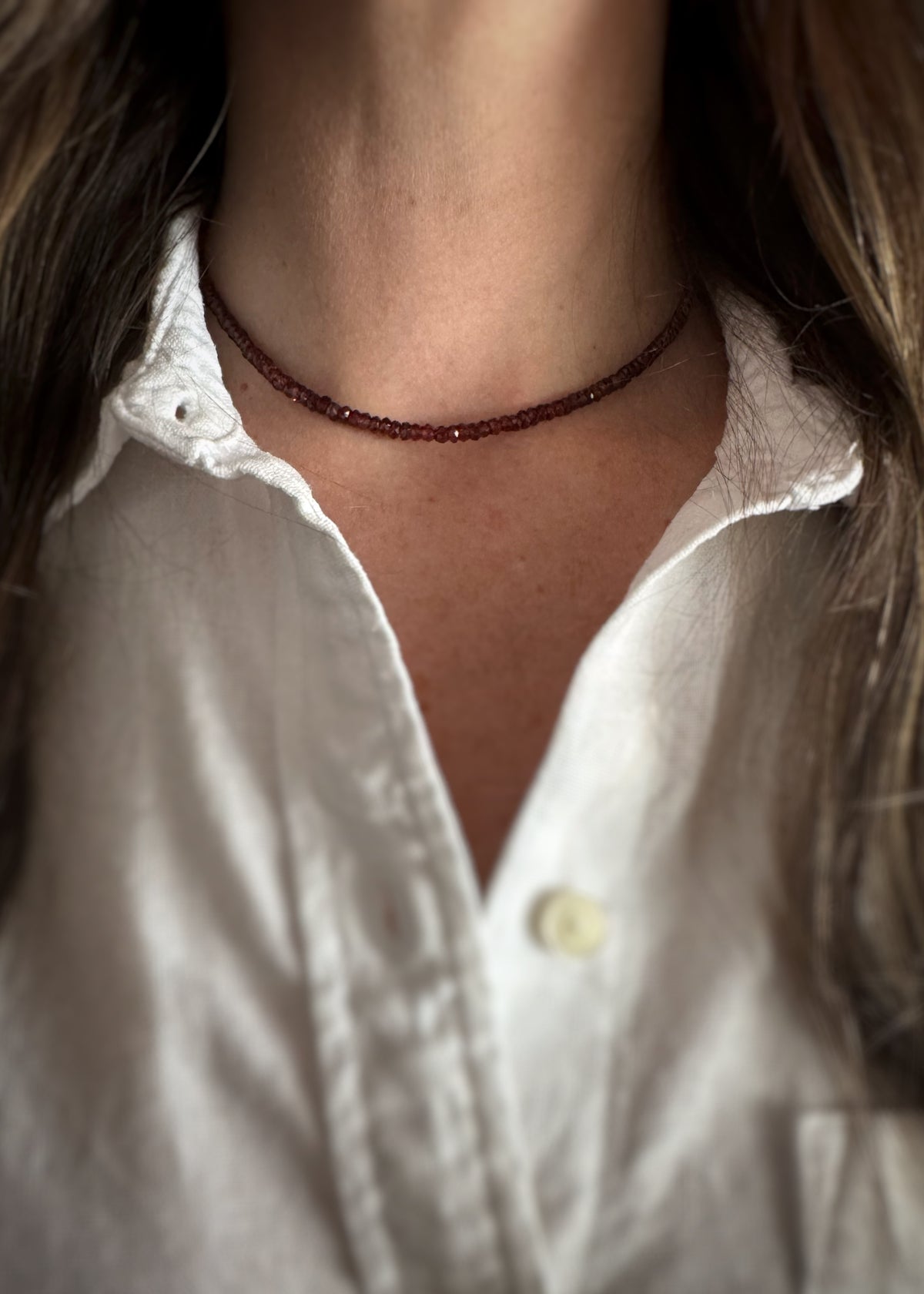 Close-up of a person wearing a genuine garnet bead necklace and a white button down shirt