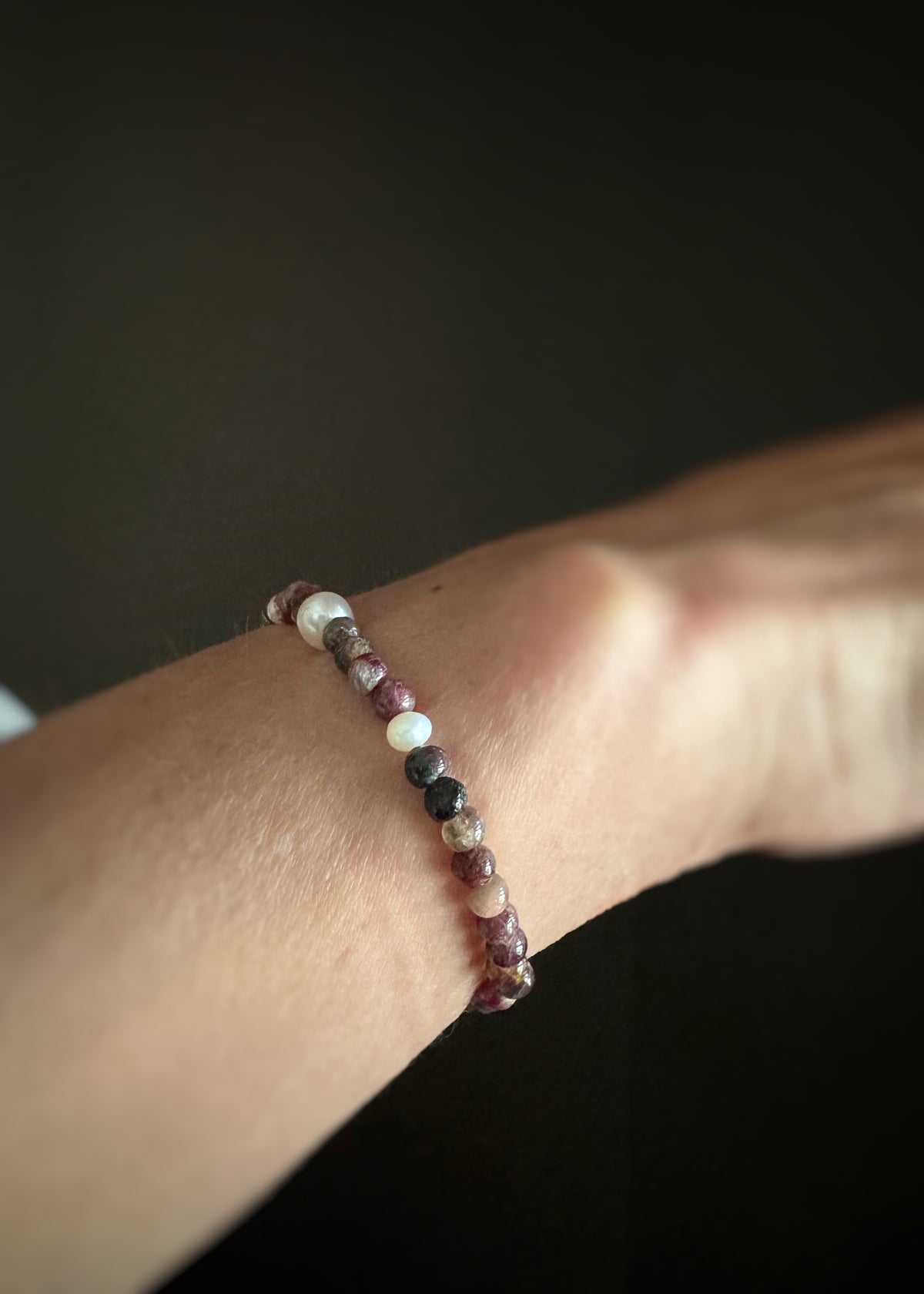 mix of pink and green tourmaline beads and pearl bracelet on a wrist with a dark background
