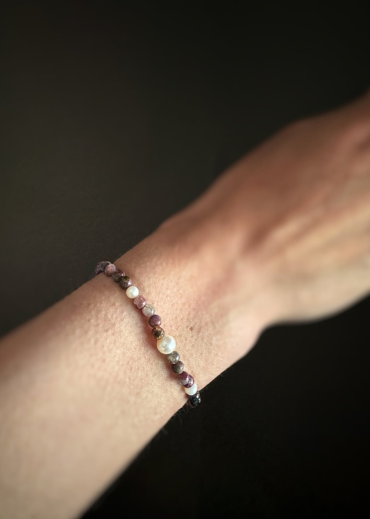 pink and green tourmaline bead bracelet with pearls mixed in on a wrist with a dark background