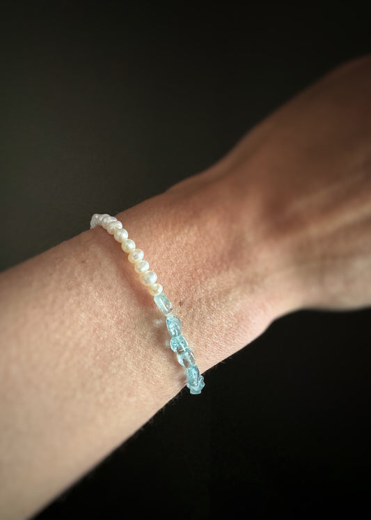 Close-up of a wrist wearing a beaded stretch bracelet with one side light blue aquamarine beads and the other side pearls against a dark background