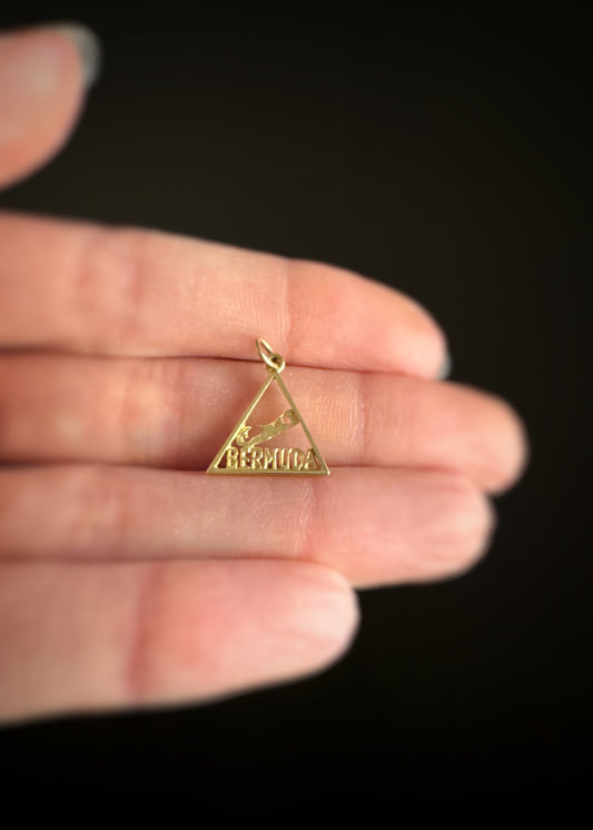 pre-owned estate 14k yellow gold  triangle pendant held between fingers against a dark background
