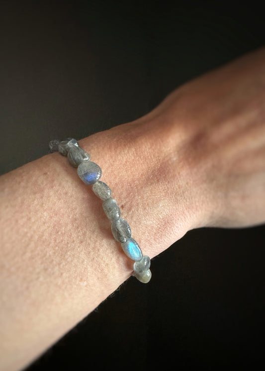  labradorite smooth chip beads strung on stretchy cord bracelet on a wrist against a dark background