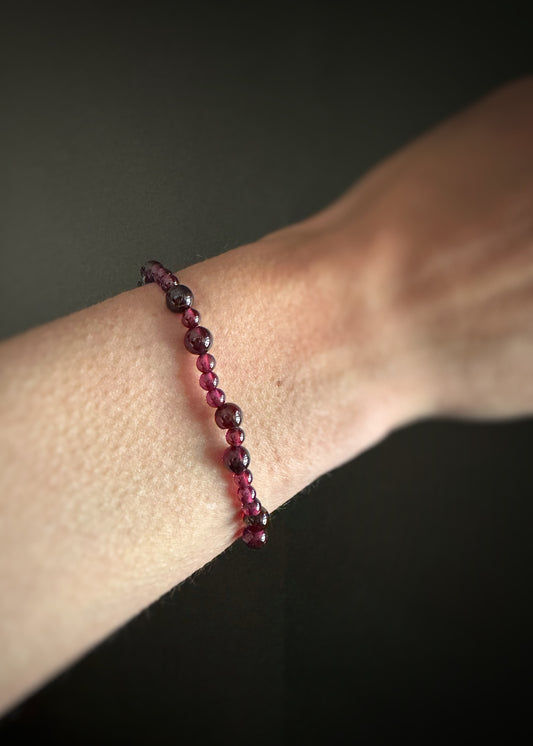 smooth garnet beads that are strung on stretchy cord bracelet on a wrist against a dark background