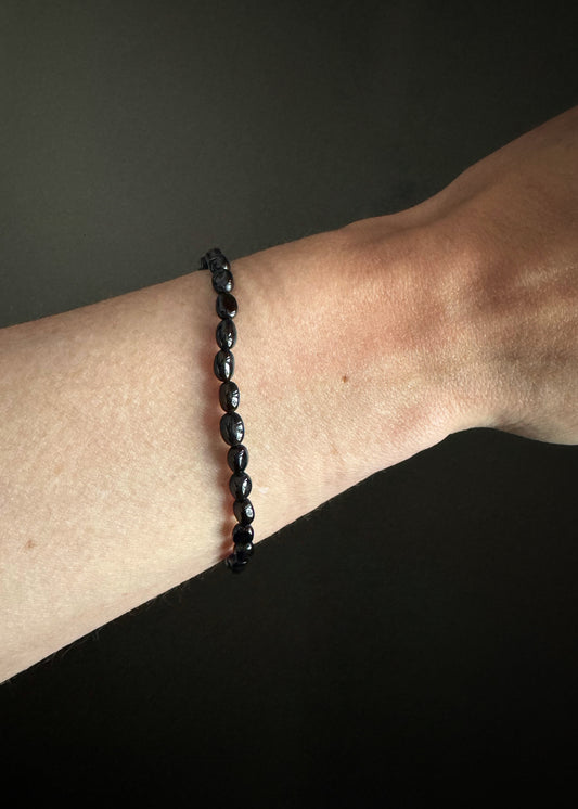 Black onyx oval smooth beaded bracelet on a wrist against a dark background