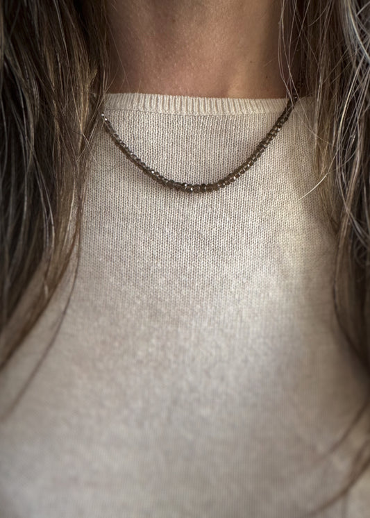 Necklace with small faceted smoky quartz beads worn by a person with long hair, against a neutral background