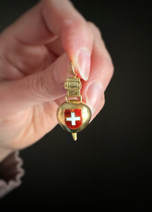 vintage yellow gold cow bell charm with a Swiss flag emblem held by a hand against a black background